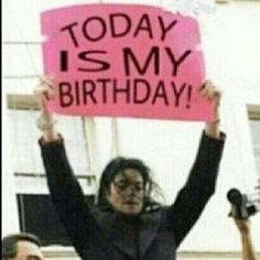 a woman holding up a pink sign that says today is my birthday with other people behind her