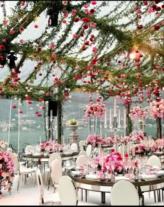 the tables are set with white chairs and pink flowers hanging from the ceiling over them