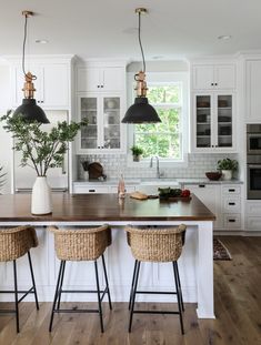 a kitchen with white cabinets and wooden counter tops, two black pendant lights over the island