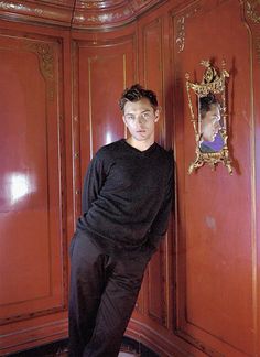 a young man standing in front of a wooden wall with a mirror on it's side