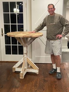 a man standing next to a wooden table on top of a hard wood floor in front of a white door