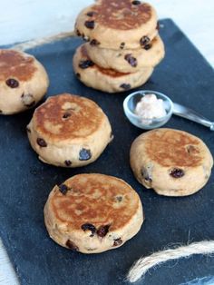 four pancakes with blueberries and butter on a black slate board next to a spoon