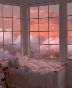 there is a bed in front of two windows that look out at the clouds outside