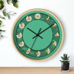 a green clock with daisies on it next to a potted plant and wall