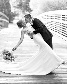 a bride and groom kissing on a bridge in black and white photo by wedding photographer