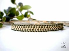 a close up of a bracelet on a white surface with green leaves in the background