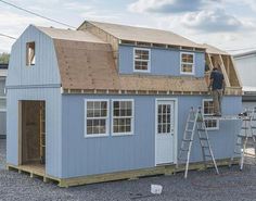 a man standing on top of a ladder next to a blue house with wooden shingles