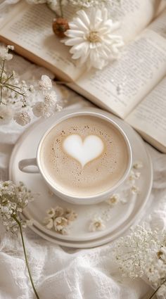 a cup of cappuccino with a heart on it next to an open book