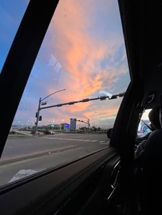 the sun is setting over an intersection with traffic lights and street signs as seen from inside a car