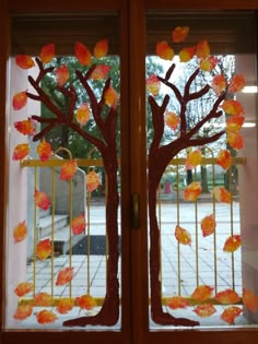 two glass doors decorated with fall leaves and tree silhouettes in front of a window