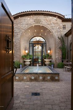 an entrance to a house with a fountain in the center and potted plants on either side