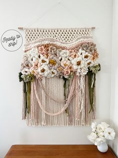 a wall hanging with flowers and beads on the bottom, next to a vase filled with flowers