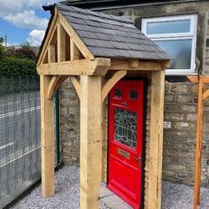 a red door in front of a stone building with a wooden arbor on the side