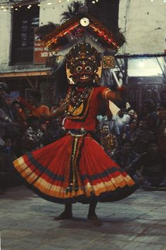 a woman in a red and gold costume dancing on the street with people watching her