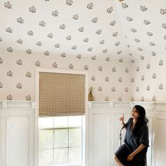 a woman sitting on a chair in front of a window looking up at the ceiling