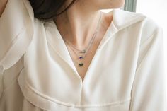 a woman wearing a white shirt with a necklace that has three different colored stones on it