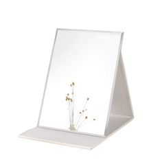 a mirror that is on top of a shelf with some flowers in front of it