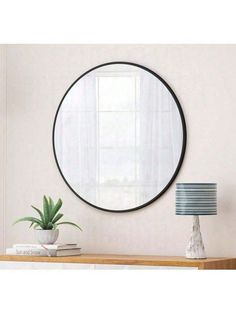 a round mirror on the wall above a table with a lamp and potted plant