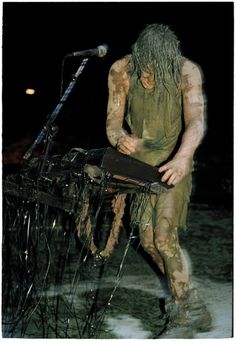 a man with long hair standing in front of a microphone and holding a book while covered in mud