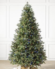 a christmas tree with lights and presents under it on a wooden floor in front of a white wall