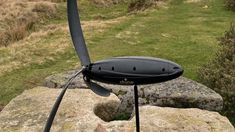 a black propeller sitting on top of a rock in the middle of a field with grass