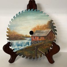 a wooden clock with a painting of a barn and waterfall on the front, hanging from a wall