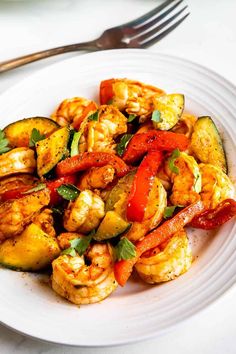 a white plate topped with shrimp and veggies next to a knife and fork