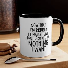 a white and black coffee mug sitting on top of a wooden table next to a spoon