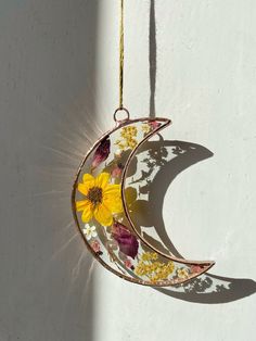 a sunflower is hanging from the side of a moon ornament on a white wall