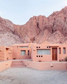 an adobe style house in the desert with mountains behind it and steps leading up to it