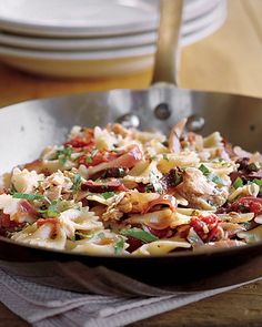 a pan filled with pasta and meat on top of a wooden table next to plates