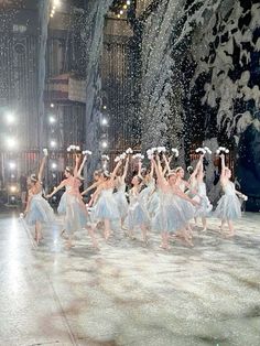 a group of dancers performing on stage in front of snow falling from the ceiling and trees