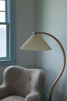 a chair with a lamp on it next to a window in a room that has wallpaper