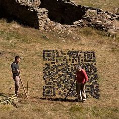 two men standing next to a large piece of art on top of a grass covered hill