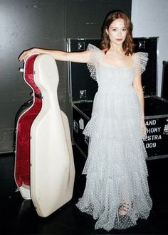 a woman standing next to a guitar case in a room with black floors and walls