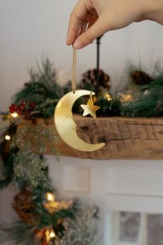 a hand holding a gold crescent ornament with stars and moon hanging from it