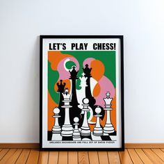 a black framed poster with chess pieces in front of it on a wooden floor next to a white wall