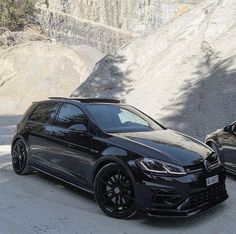 two black cars parked next to each other in front of a mountain side area with trees