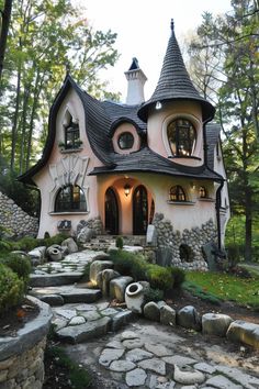 a pink and white house in the middle of some trees with lots of rocks around it