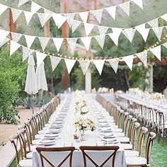 a long table is set up with white linens and wooden chairs for an outdoor party