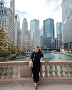 a woman standing on the side of a bridge next to a river and tall buildings