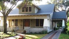 a small house with two front porches and trees in the foreground, on a sunny day