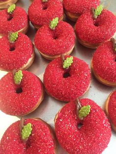 red donuts with sprinkles and leaves on them are arranged in rows