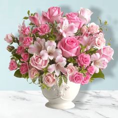 a white vase filled with pink roses and greenery