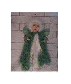 a doll with green hair and wings hanging on a brick wall