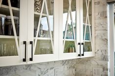 a kitchen with marble counter tops and white cabinets in front of a glass doored window