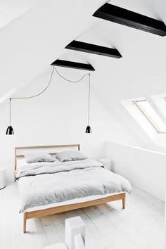 a bed sitting under three black lights in a white room with slanted ceiling beams