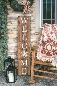 a wooden welcome sign sitting next to a rocking chair and christmas wreath on the front porch