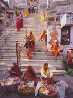 several women sitting on the steps in front of a building with flowers and baskets full of food