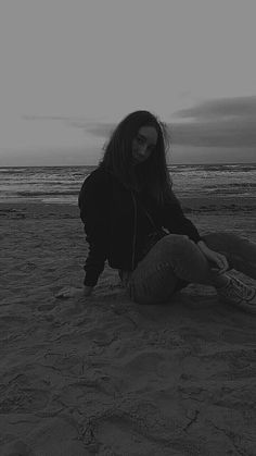 a woman sitting on top of a sandy beach next to the ocean with headphones in her ears